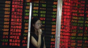 A Chinese woman stands behind a glass panel near stock prices displayed on a board at a brokerage house in Shanghai, China, Monday July 6, 2015. Shares in big Chinese state companies rose Monday following weekend promises of government action to halt a slide in stock prices but many others sank as jittery small investors looked for ways to cut their losses. (Chinatopix Via AP) CHINA OUT